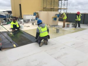 Applying adhesive to roof to adhere the TPO roofing material